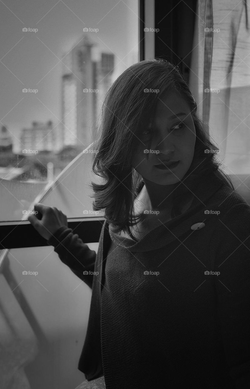 asian woman sitting behind a hotel room window in singapore