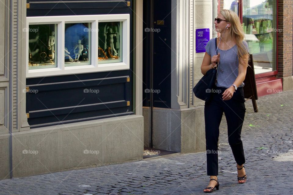 Street Shot Of Blond Woman Walking Down The Street With Earbuds