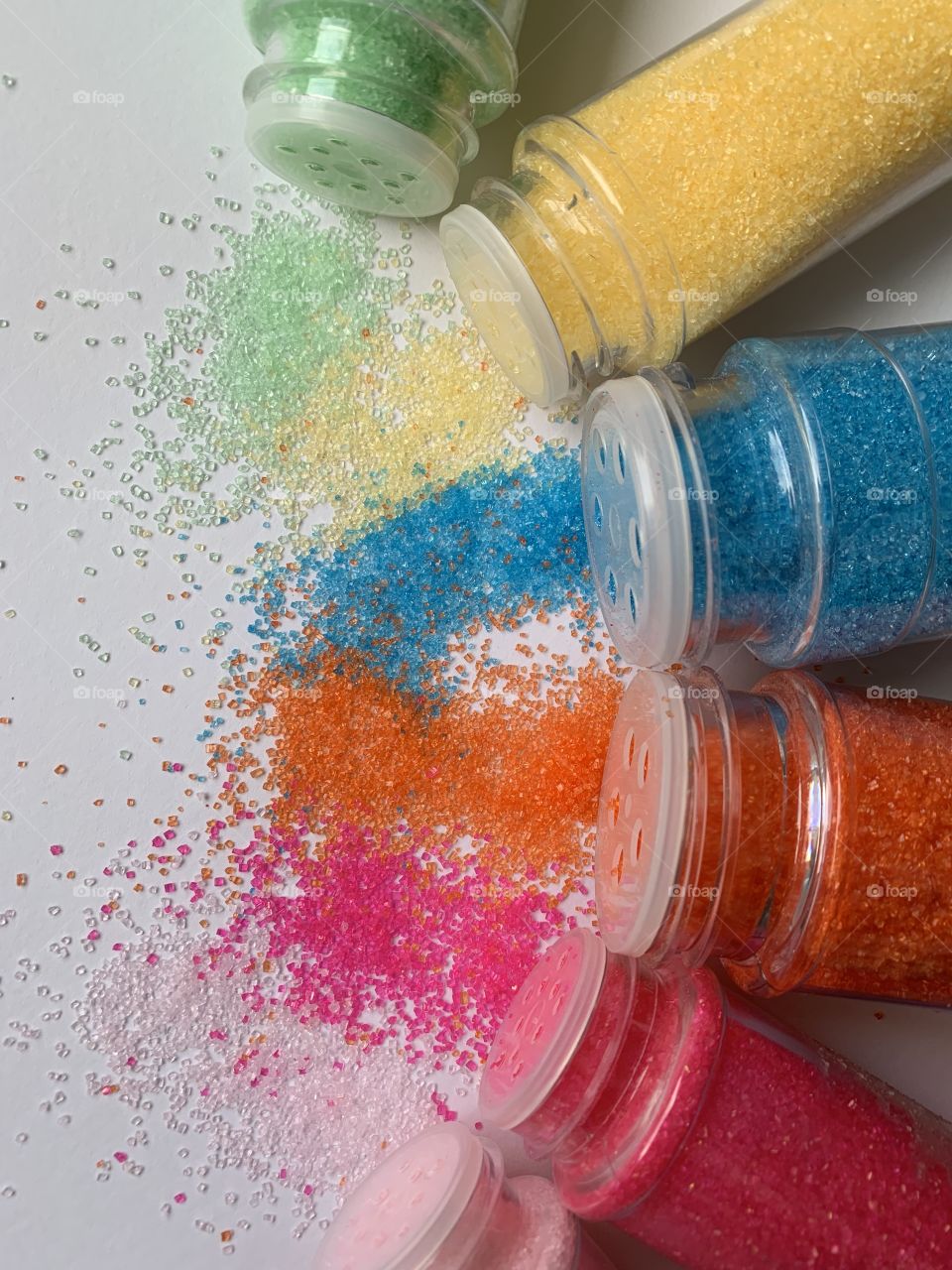 Bright colored sugar sprinkles spilling out of their bottles onto a white surface