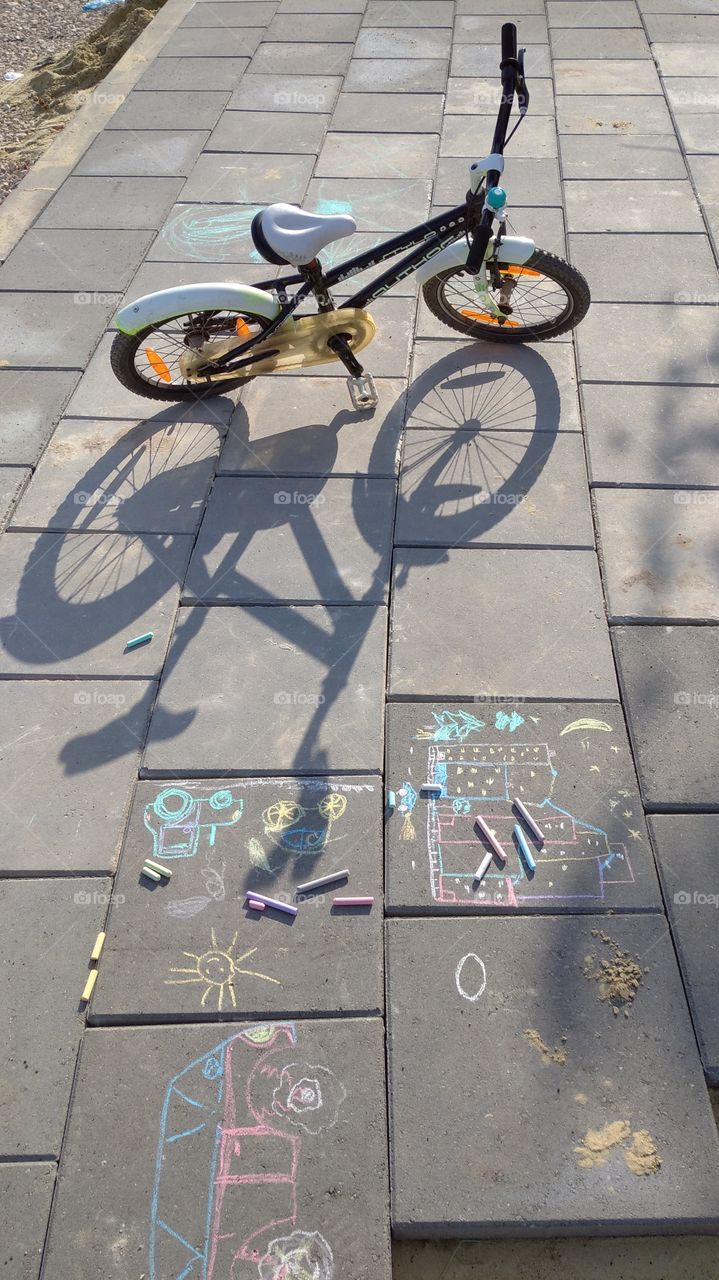 Summer games. Kid's bike and chalk drawings on the street pavement.