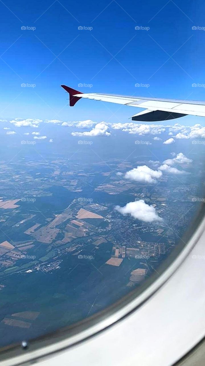 View of the ground from the plane's window.  Land.  Blue sky.  White clouds.  Airplane wing