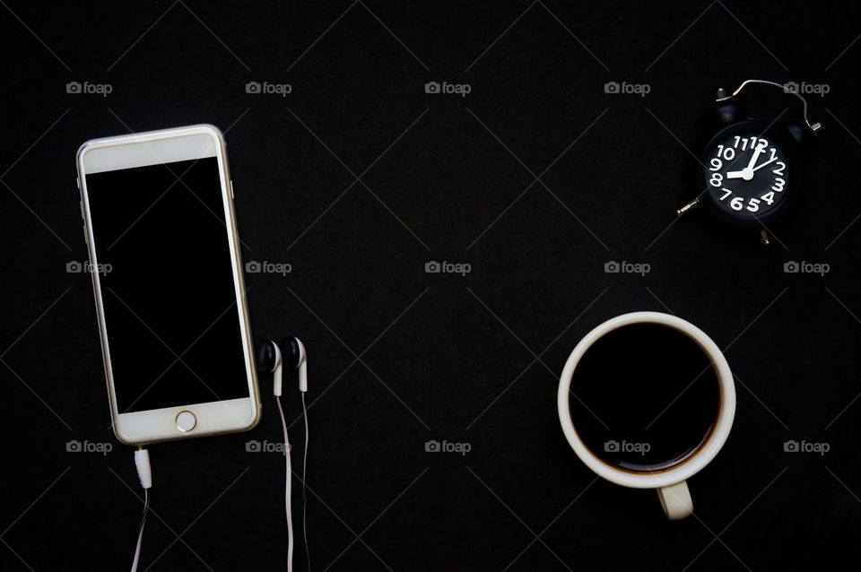 Smartphone and coffee, alarm clock on black background with copy space 