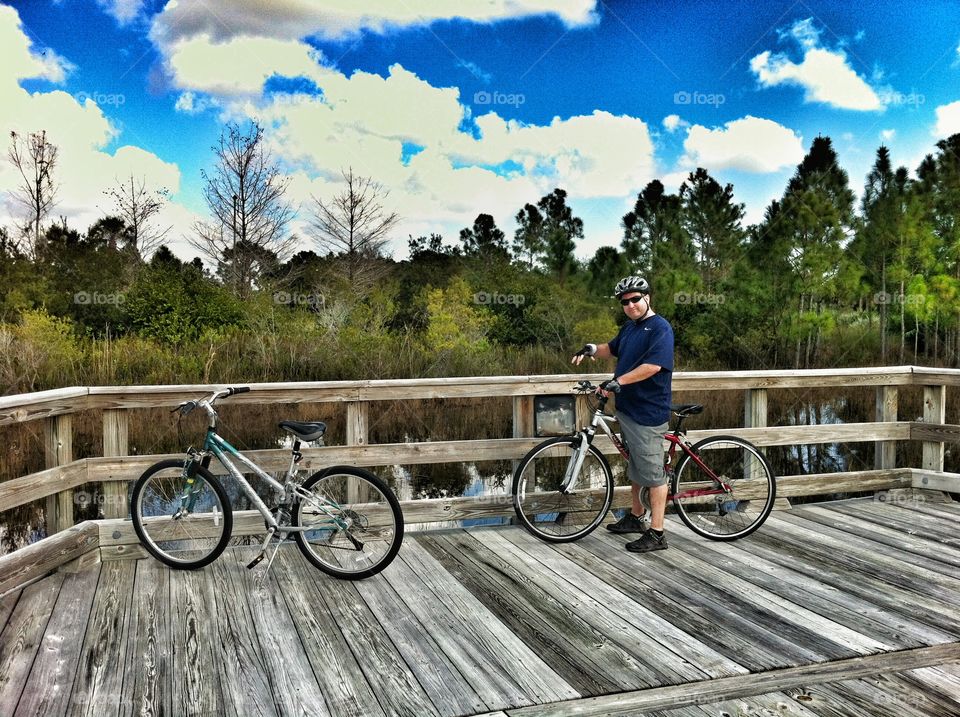 Man with bicycle near railing against cloudy sky