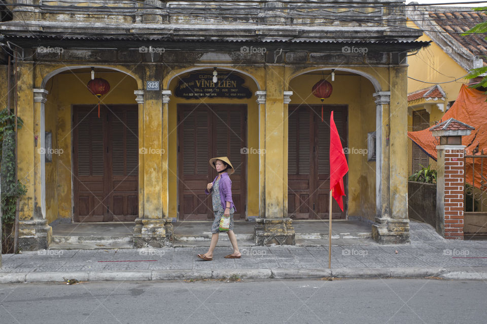 typical scene in Hoi An ancient town, old lady wearing conical hat and traditional costume walking in the street in central Vietnam