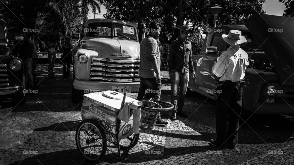 Homens, picapes da antiguidade e carrinho de picolé.