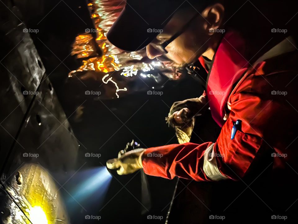 An emergency responder inspecting a marine structure at night, holding a torch light in his hand. 