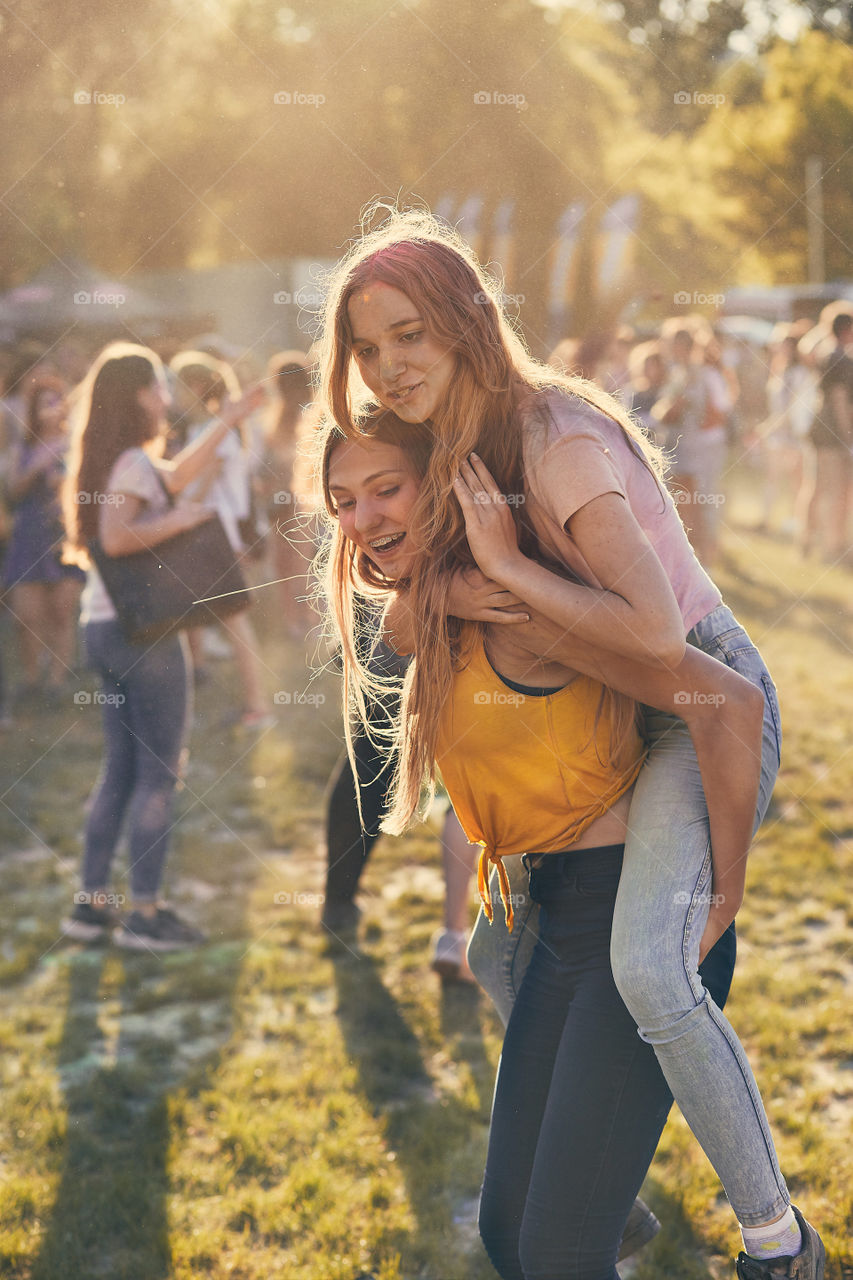 Portrait of happy smiling young girls with colorful paints on faces and clothes. Two friends spending time on holi color festival. Real people, authentic situations