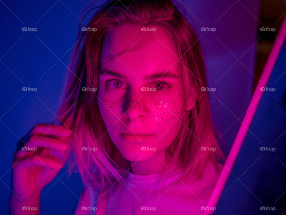 Young woman selfie portrait in pink and blue neon light and glitter freckles 