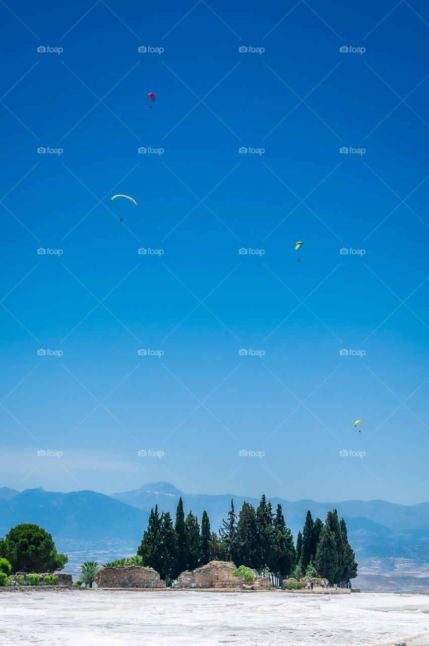 Gliders in the sky above white as snow plateau of the Pamukkale Terraces known as the Cotton Castle in Turkey.