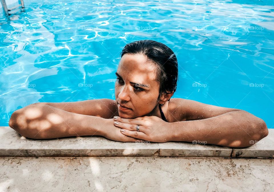 Portrait of young woman with wet hair, relaxing on edge of swimming pool