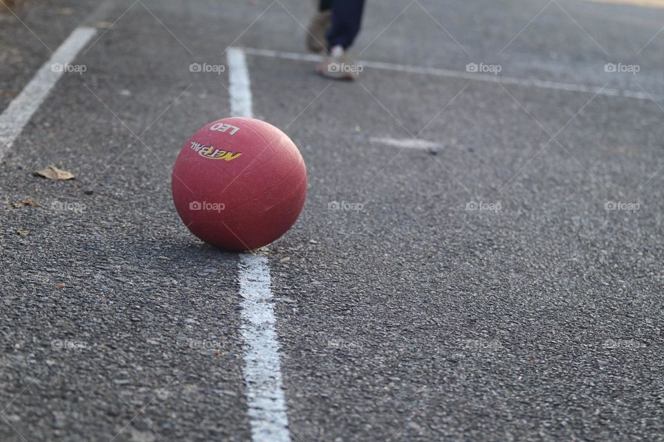 Close up view of a red ball on a white line in a basketball court and someone walking towards it 
