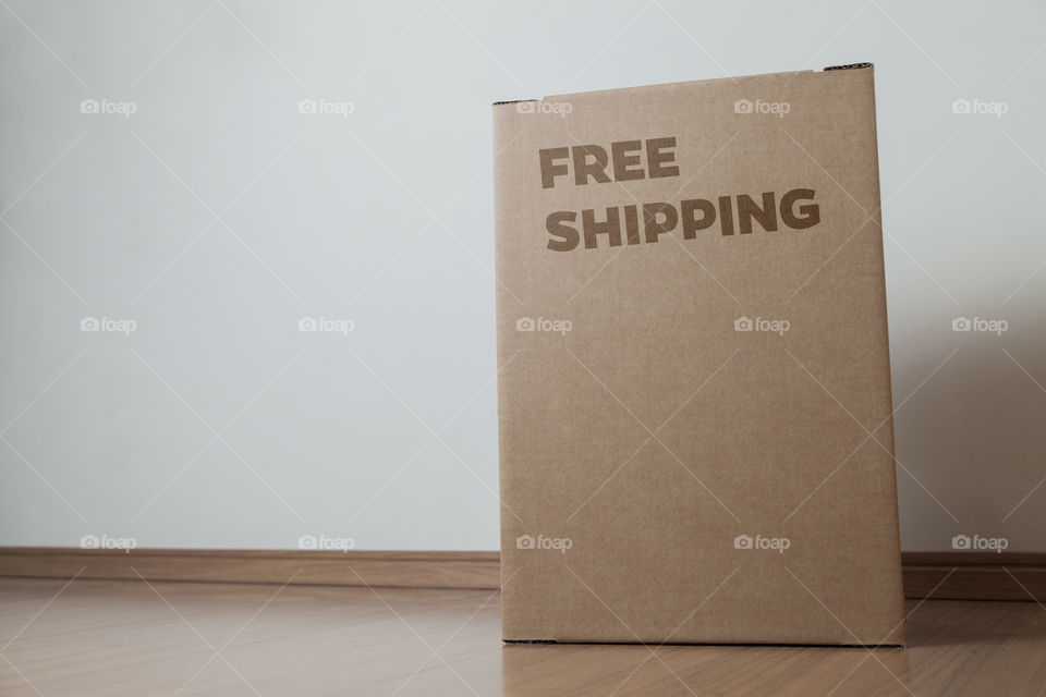 Cardboard box with written free shipping order placed on the floor in front of the house door at the time of delivery with the house door in the background. free delivery concept. transport concept.