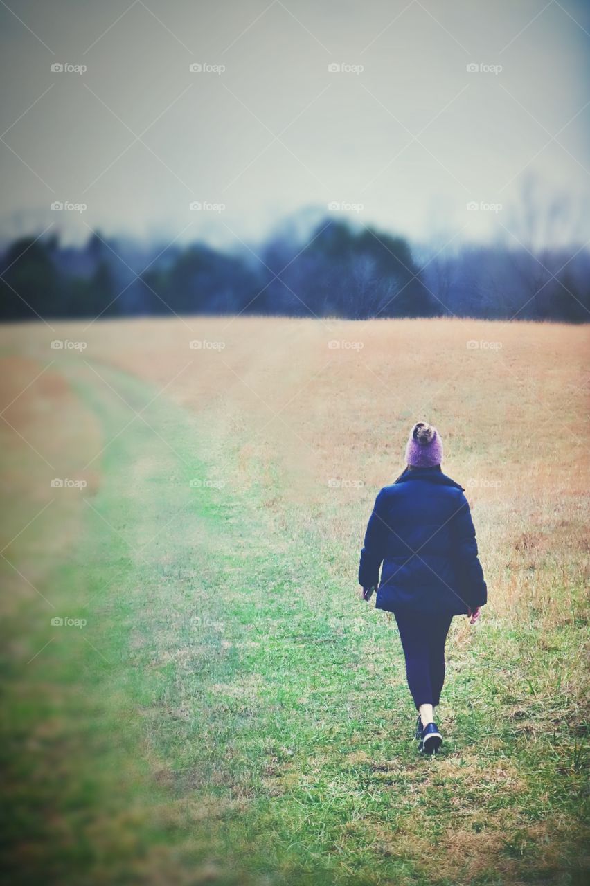 An athletically dressed female walks independently in a field on a cold winter day