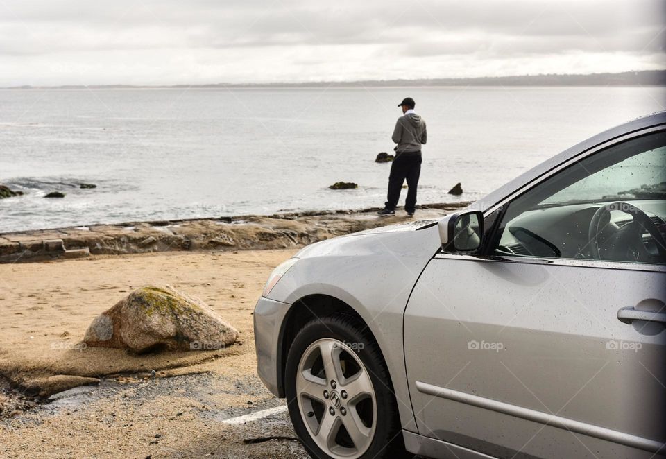 Silver sedan parked seaside, driver in the background.