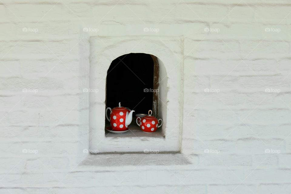 a red teapot and a polka dot cup stand in the window of a white wall