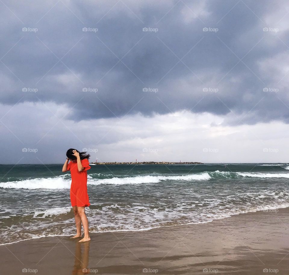 Young girl in red next to sea before storm 