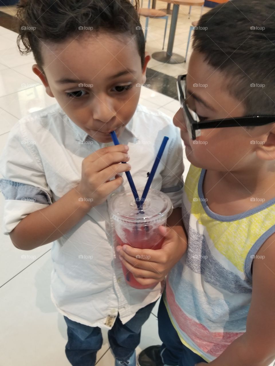 Two boys sharing a cold beverage out of a straw on a hot summer day.