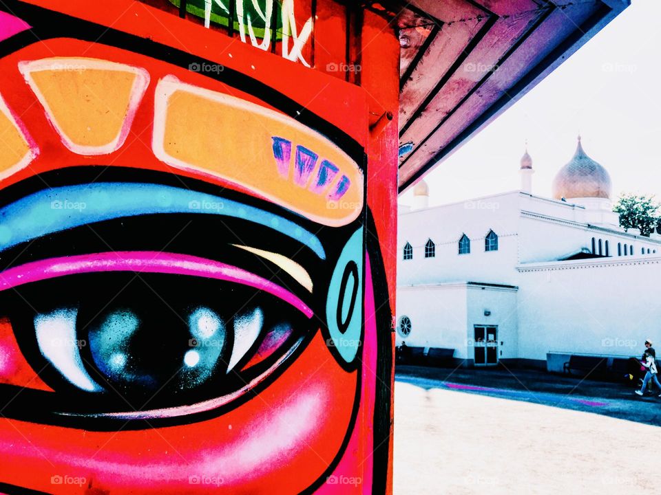 Painted eye in the foreground standing in front of a white building 