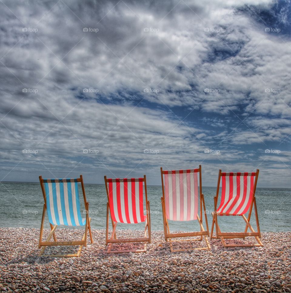 Four colourful deckchairs facing the ocean on an empty beach.