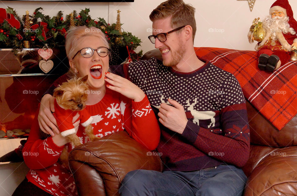 A young couple in Christmas knit ware and a small dog in a Christmas