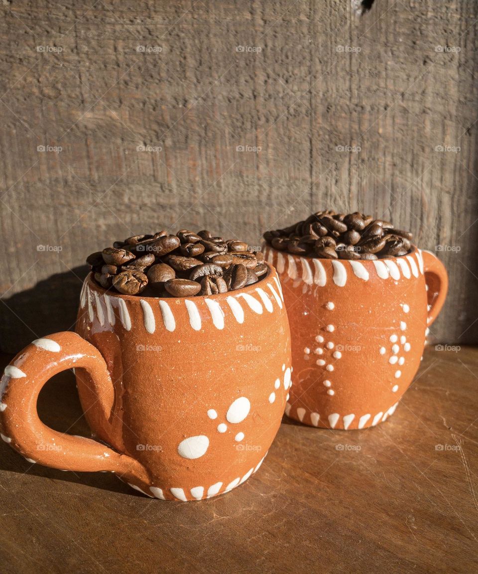 Coffee beans in Portuguese terracotta mugs with a wood background 