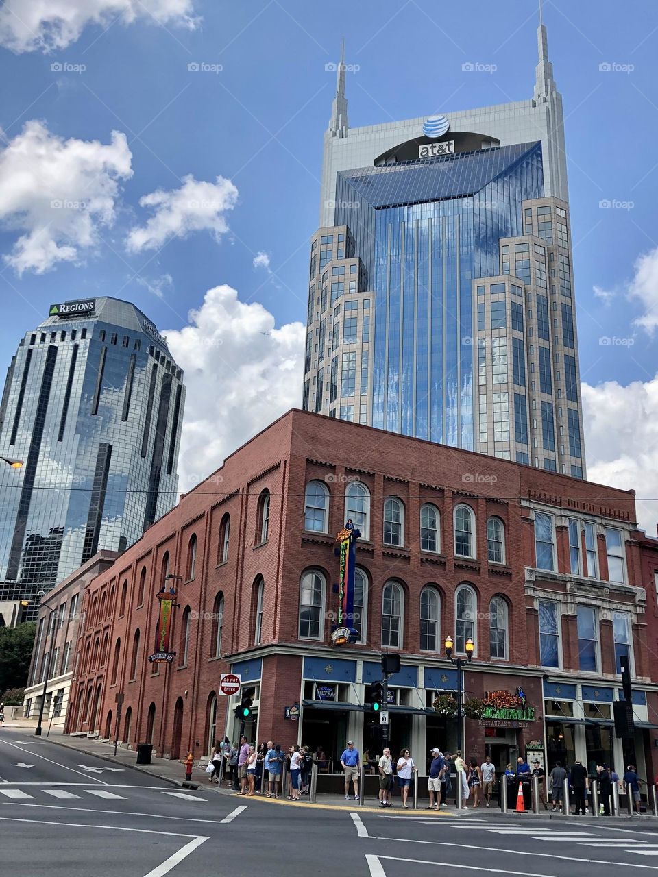 Queue crowd lining up to get into Margaritaville bar in downtown Nashville Tennessee in front of Batman AT&T building mirror clouds sky sunny summer day skyscrapers city skyline