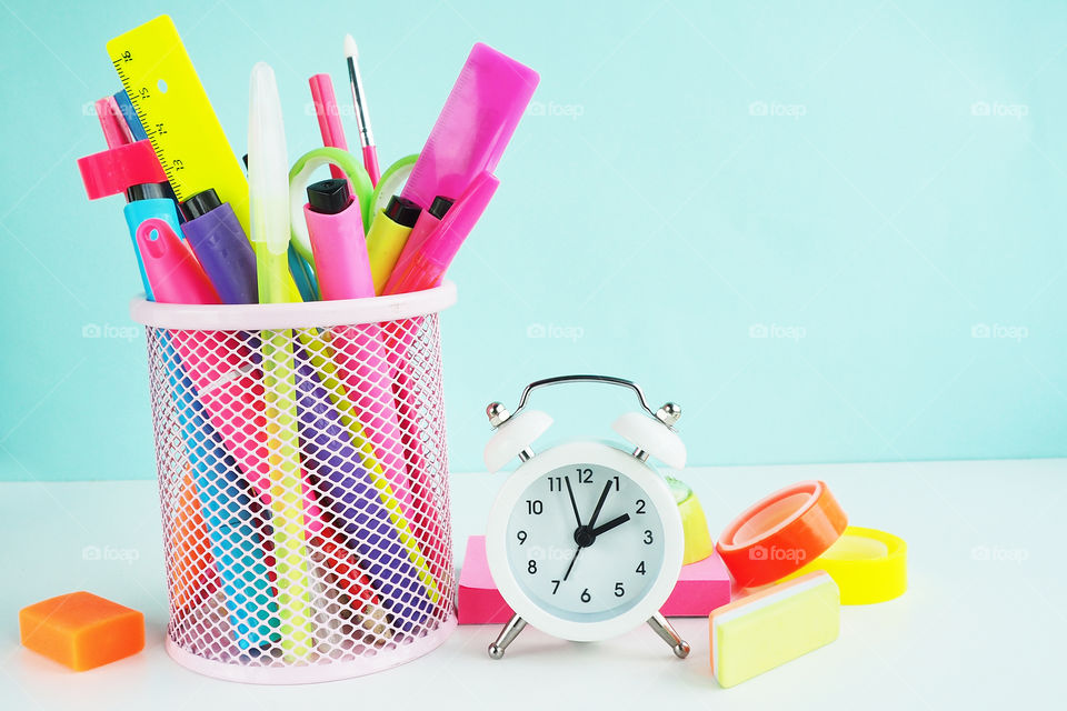 bright colored markers and pencils in a cup and a white alarm clock