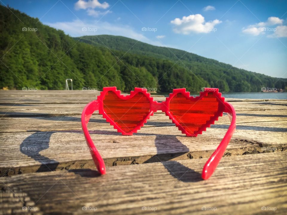 Heart shaped sunglasses on wooden pontoon near the lake