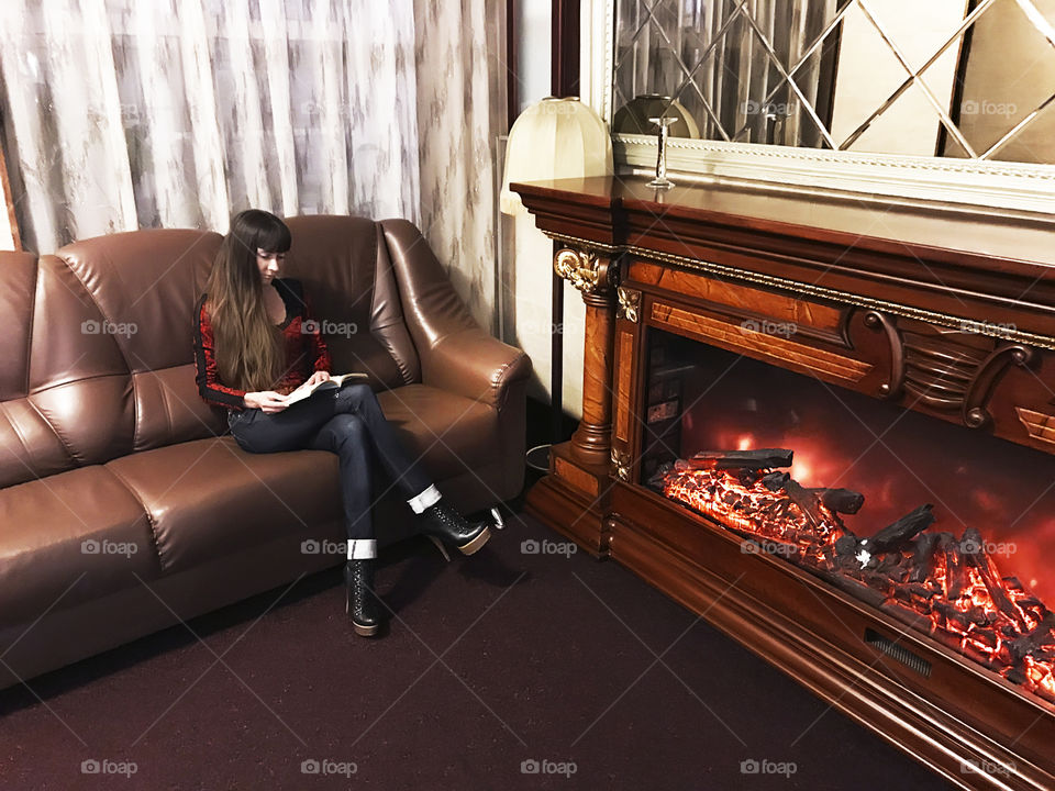 Young woman reading a book at the fireplace at home 