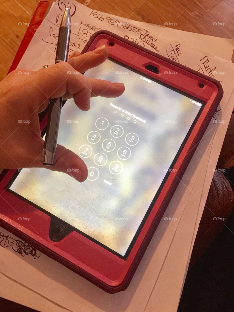 My pink iPad on the password screen with my hand and a pen
