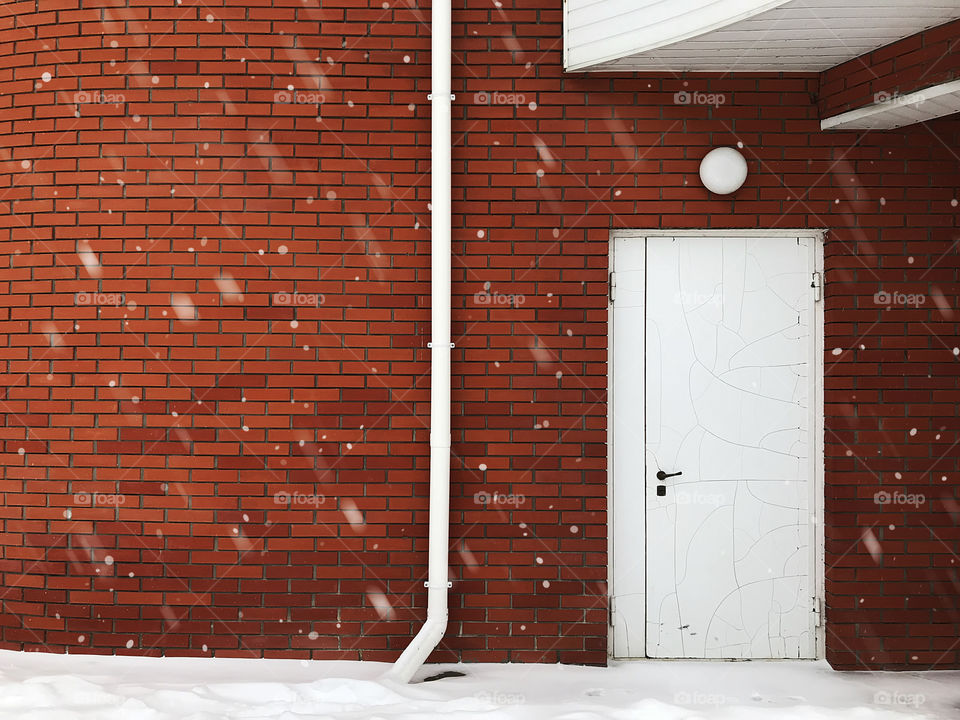 White snow in front of red brick wall with white door and white sink 