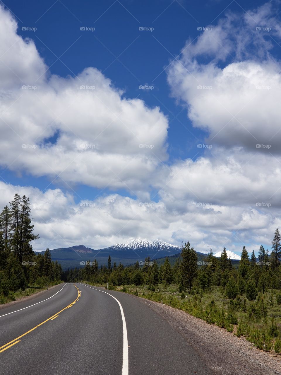 Summer road trip along a backroad in the Deschutes National Forest in Central Oregon with a beautiful blue sky full of fluffy white clouds.