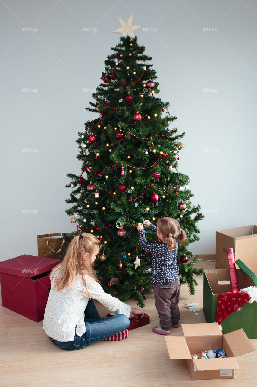 Young girl and her little sister decorating Christmas tree at home