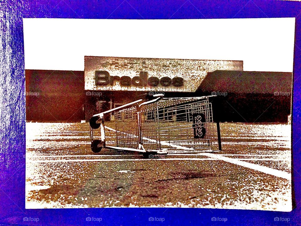 “Bradlees”, is a department store that is part of a strip mall on “Cape Cod”, “Massachusetts”. This colorized photo of a shopping cart laying on its side outside the store is a veritable work of art. 1980. Hypnotic Productions
