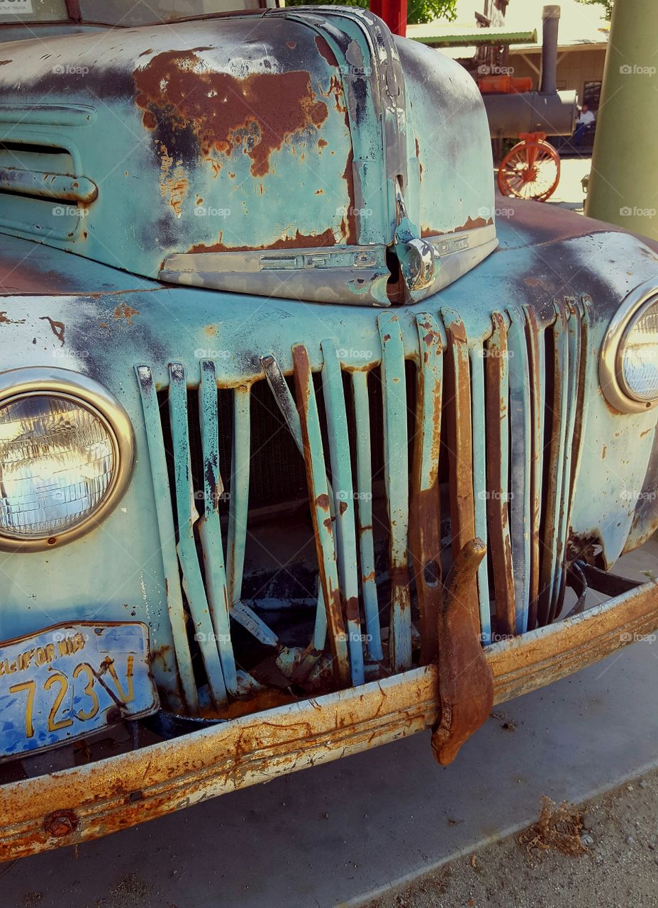 An old vintage Ford truck sits in a history park on display pulled into an old gas station