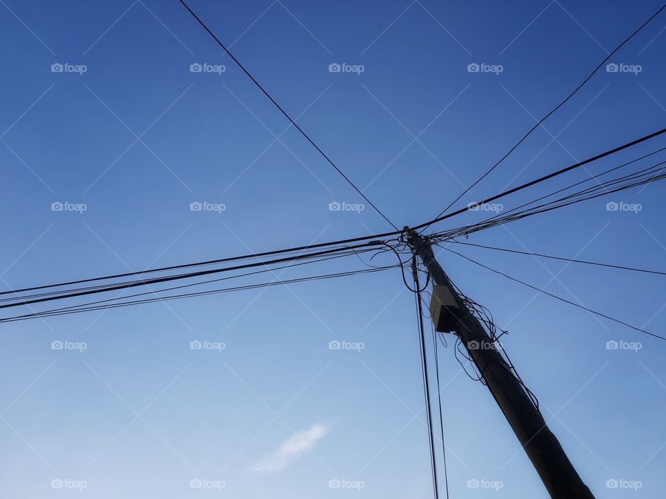 an electrical pole with long cables is seen from the ground.