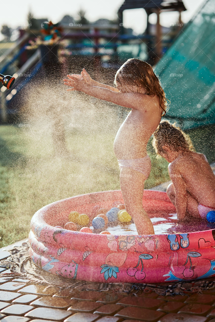 Little cute adorable girls enjoying a cool water sprayed by their father during hot summer day in backyard. Candid people, real moments, authentic situations