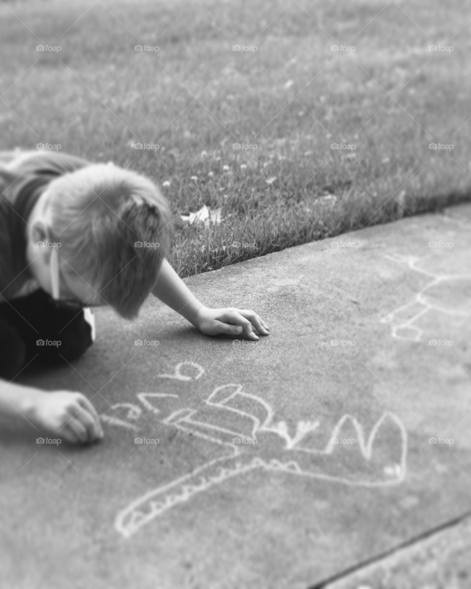 Little boy drawling with chalk outside. 