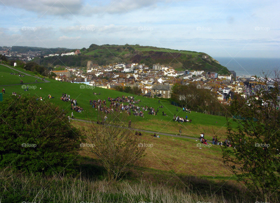 A view of the east hill from the west hill in Hastings, UK. Many people are gathered on the grass and the old town can be seen behind them