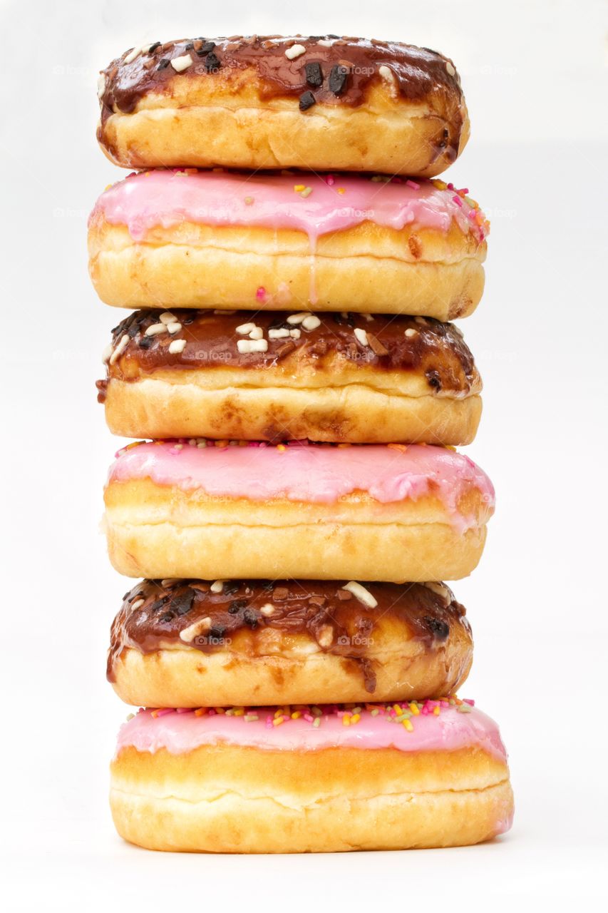 A tall stack of donuts with pink and chocolate icing on a white background.