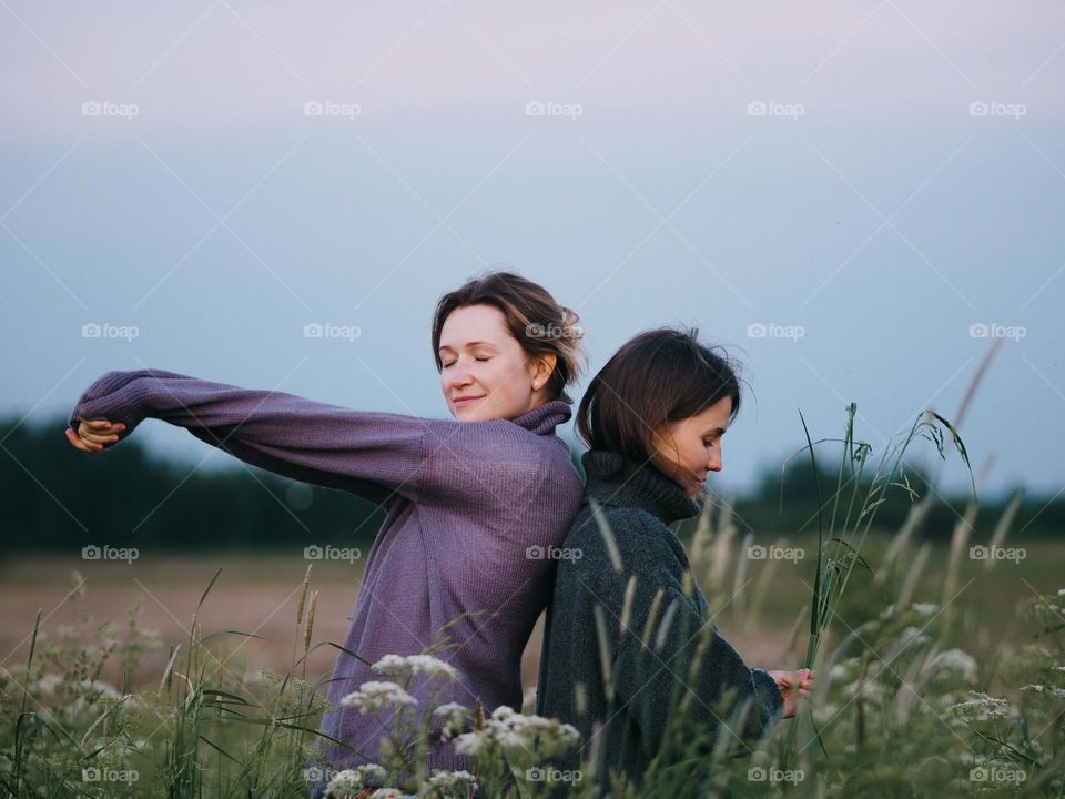 Two beautiful girlfriends standing in a green field on a summer day