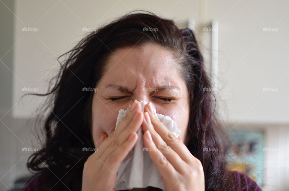 Woman blowing her nose hard into a tissue at home