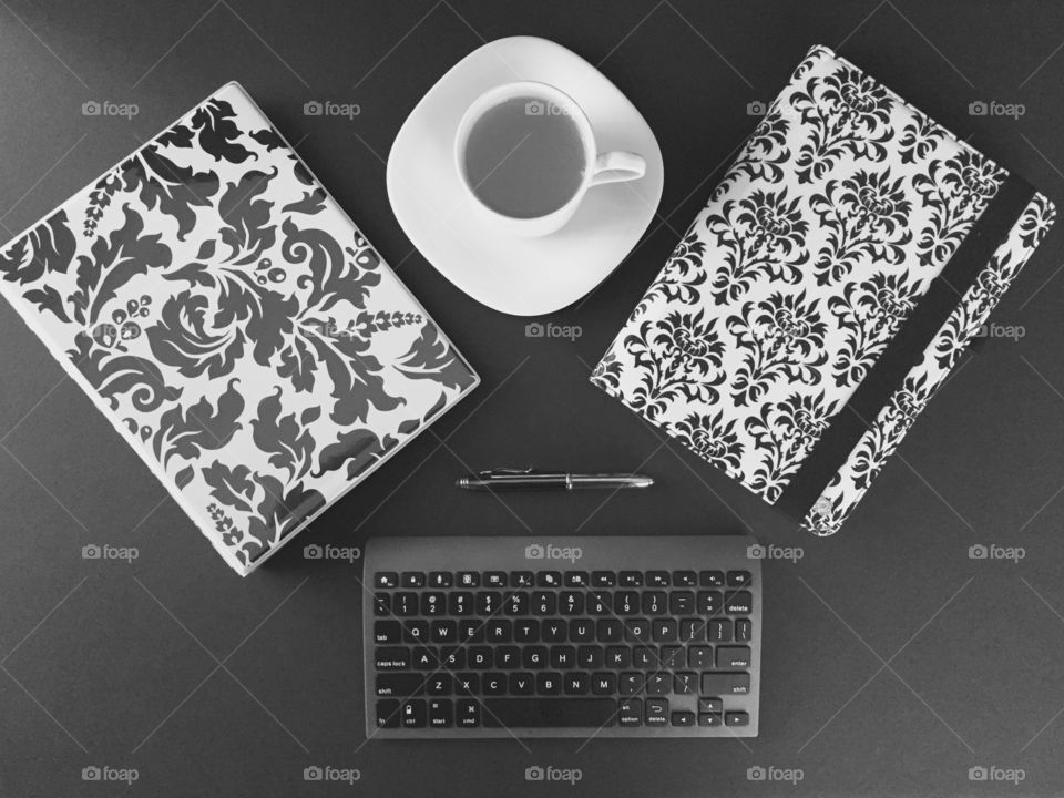 Top view desk - tablet, binder, Bluetooth keyboard, stylus, tea in cup with saucer in black and white