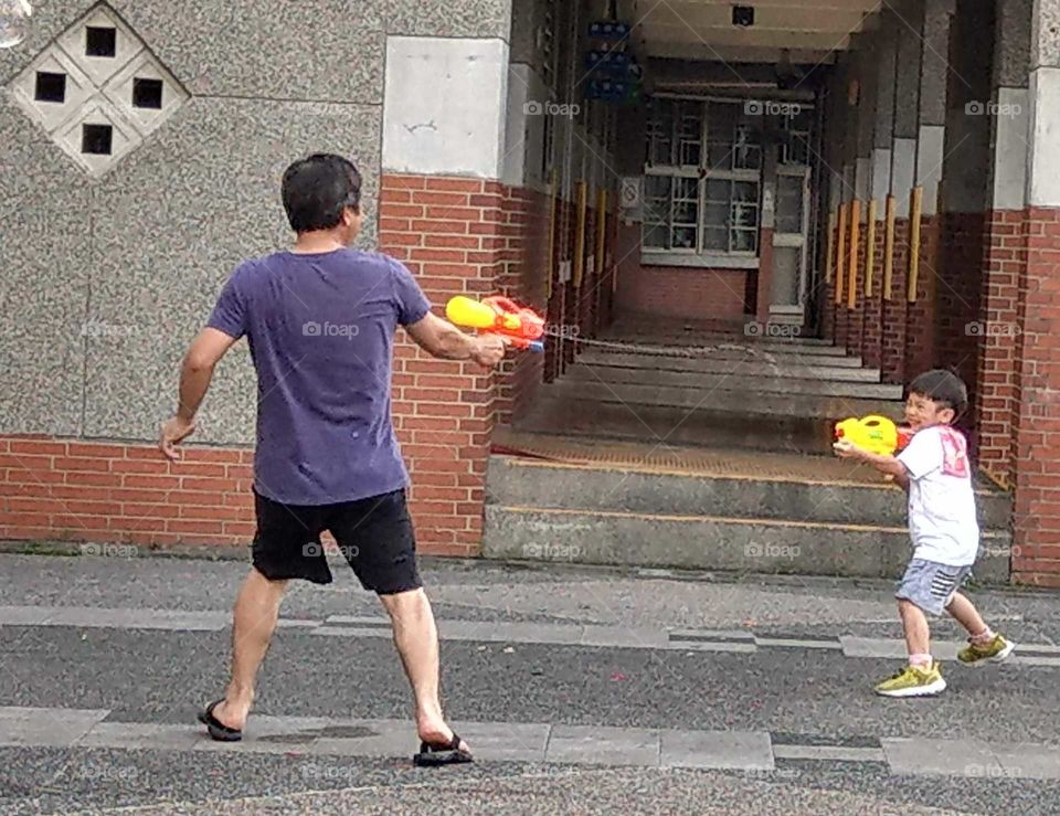 The memories of summer: boy playing water gun with his father during summer vacation, very happy.