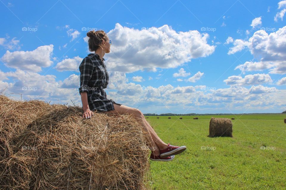 the girl is sitting on a haystack in the field