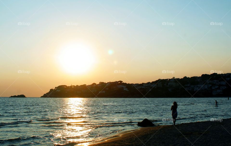 Beach while sun sets. A woman looks in the sun direction.