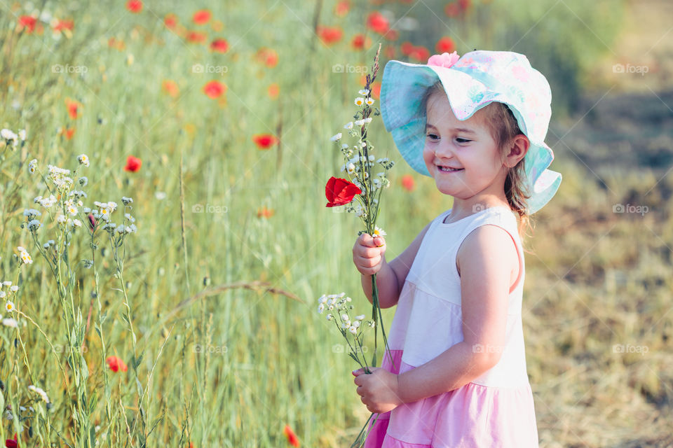 Lovely little girl in the field of wild flowers. Cute girl picking the spring flowers for her mom for Mother's Day in the meadow. Girl holding bouquet of flowers. Spending time close to nature