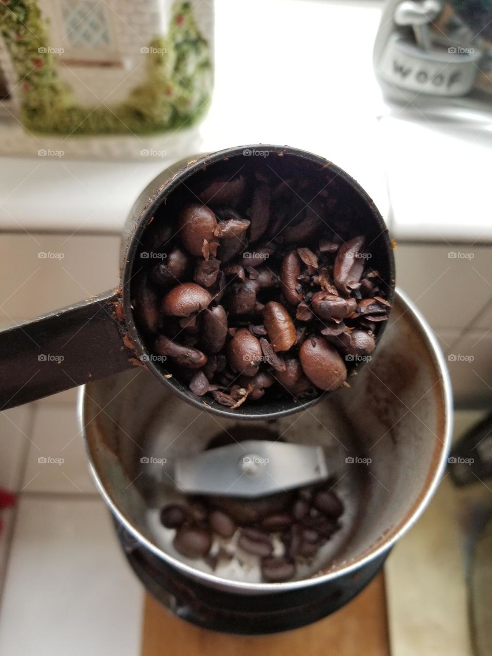 Coffee Beans in a Measuring Cup being poured into a Grinder