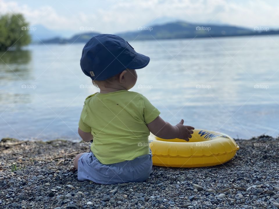 a little boy sits by the lake and enjoys a warm summer day