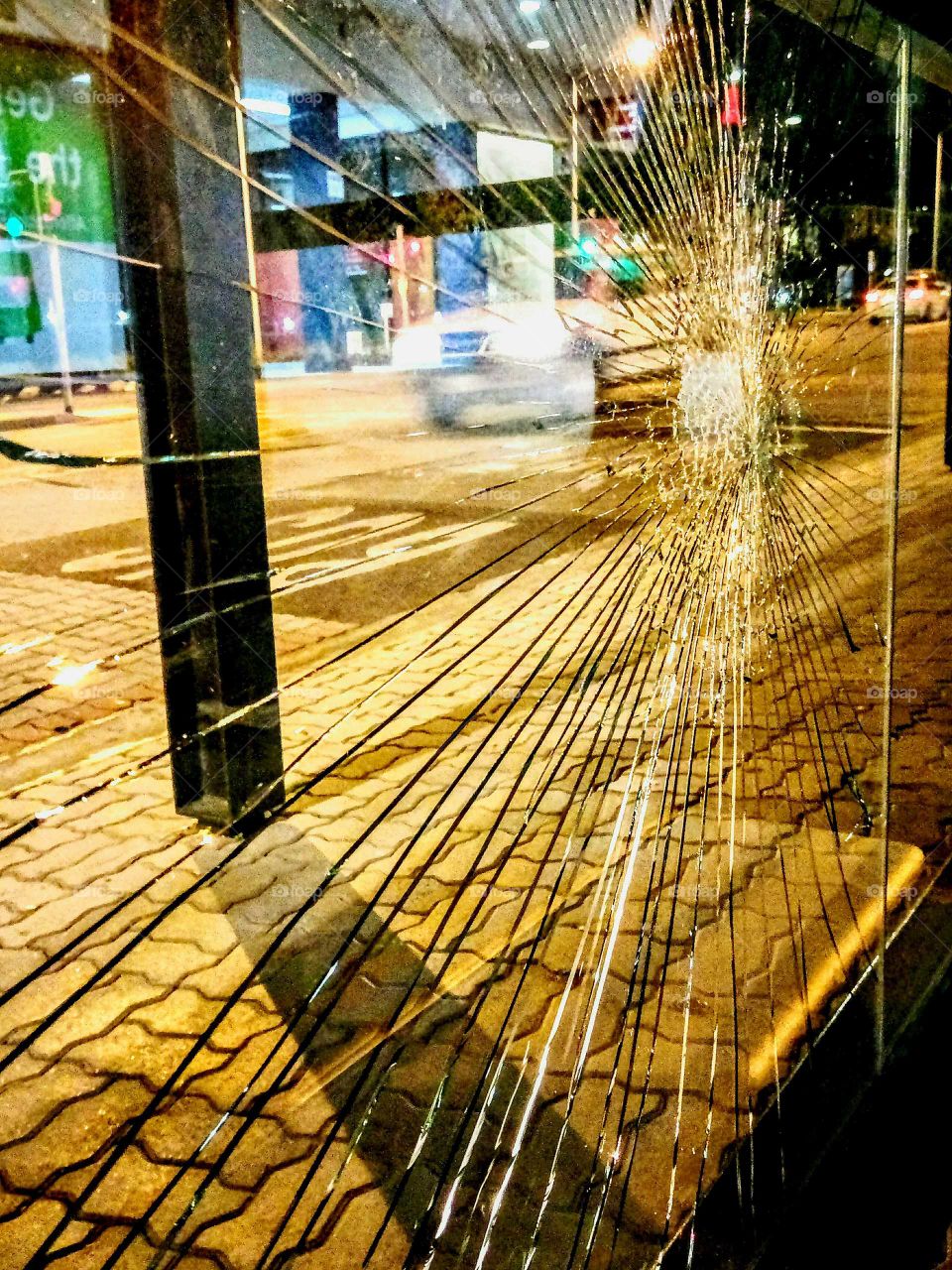 passing vehicle shot through shattered glass of bus shelter